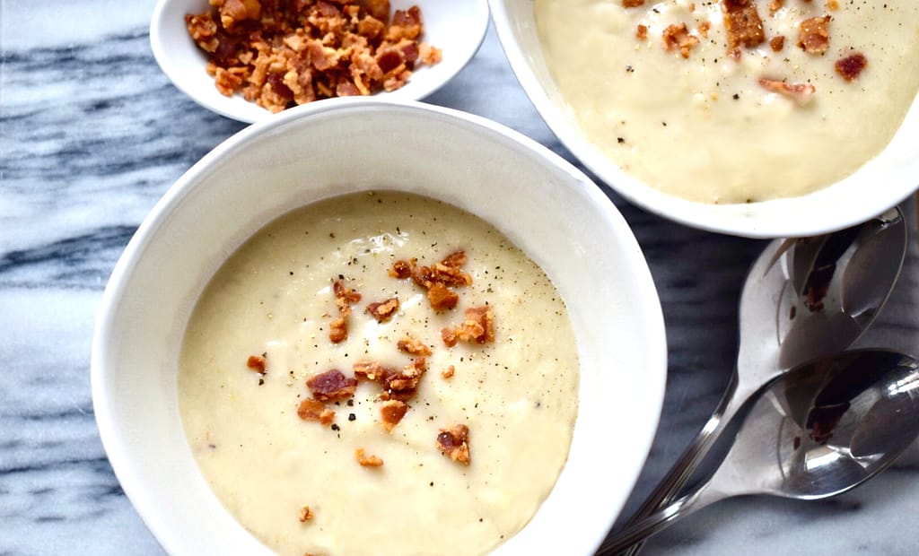 Two bowls of cauliflower soup with crumbled bacon and a side of crumbled bacon.