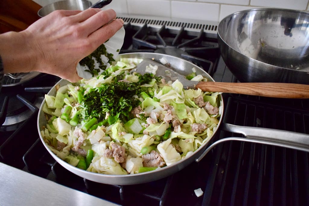 Adding chopped basil to skillet of pork stir fry.