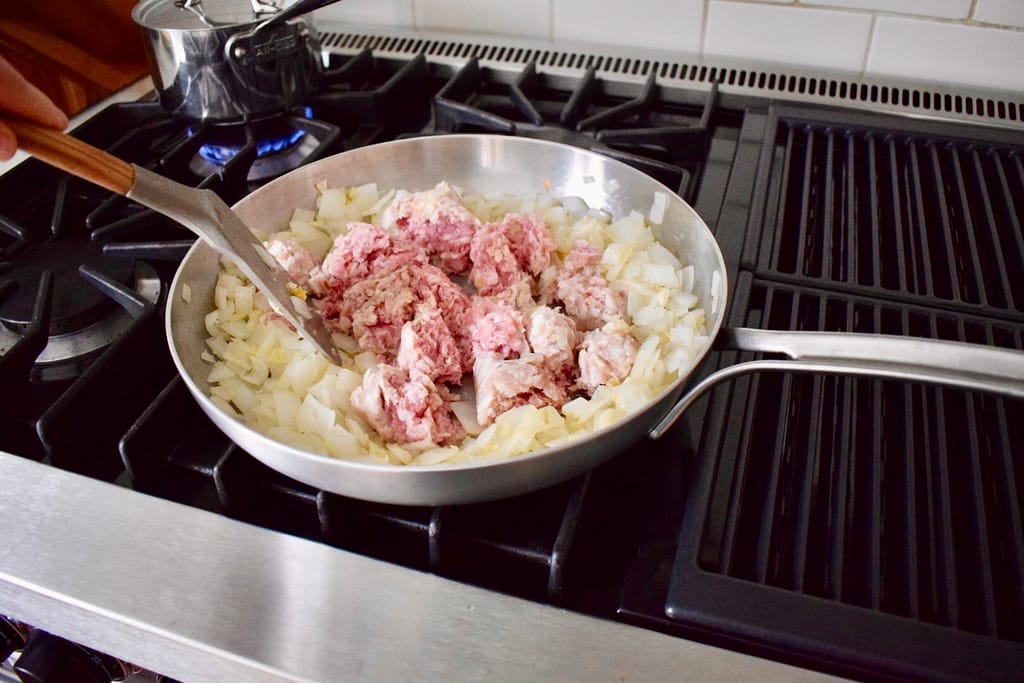Adding ground pork to pan and breaking it up with a spatula.