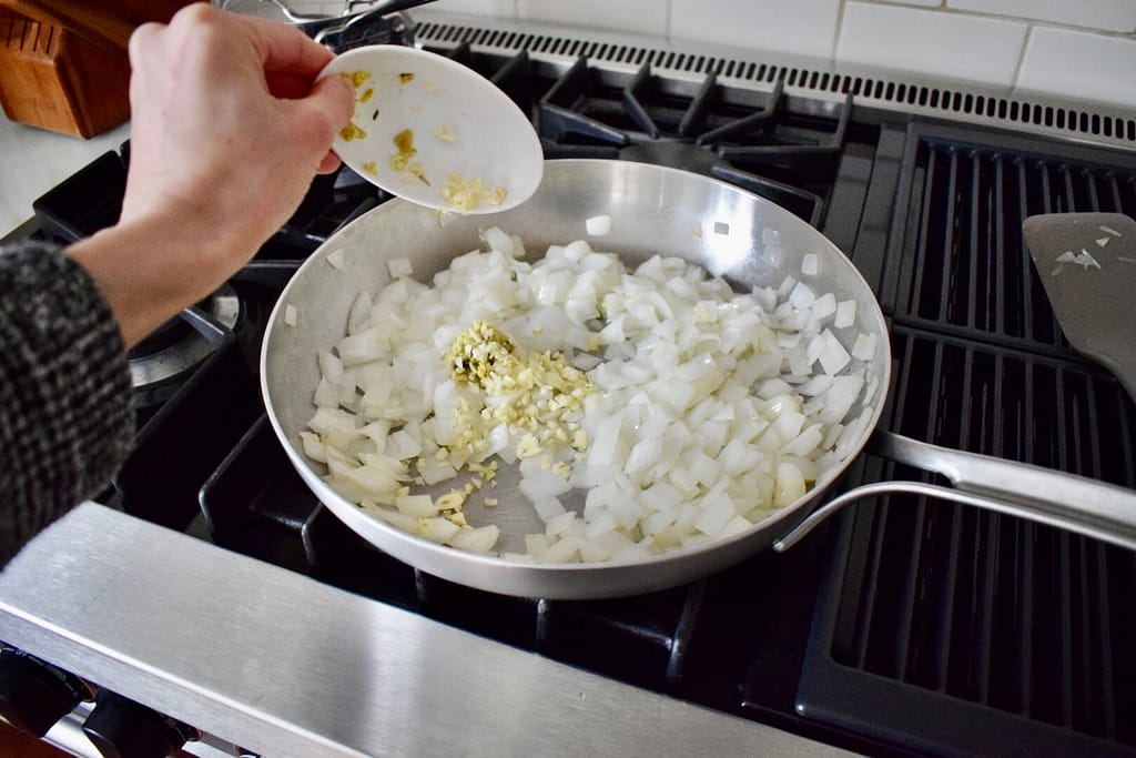 Adding minced garlic and grated ginger to sauteed onion.