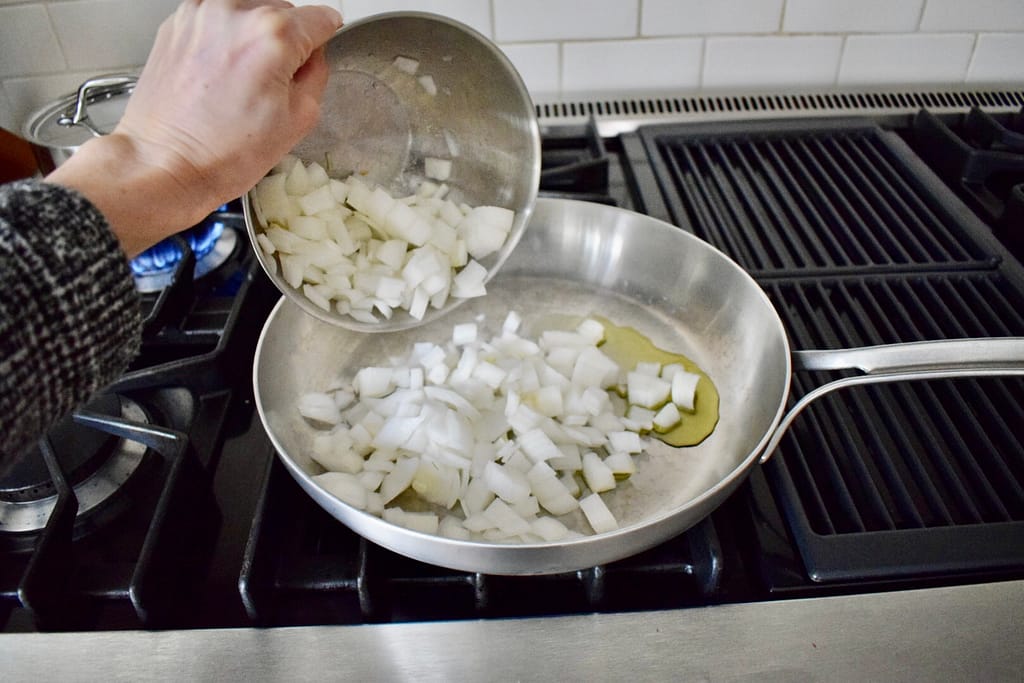 Chopped onions being added to hot skillet with avocado oil.