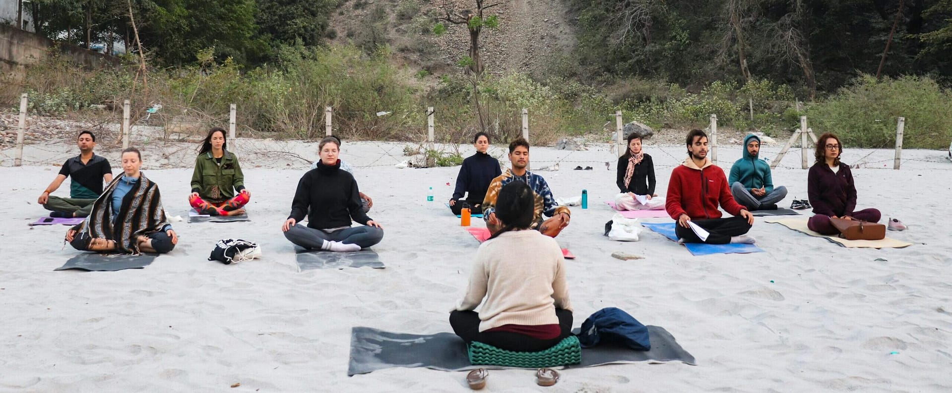 group meditating on the beach with a hillside in the background