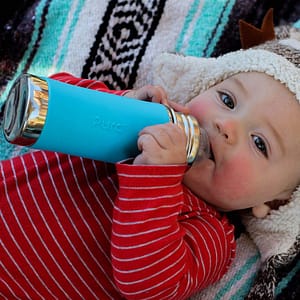 Baby holding blue Pura bottle.