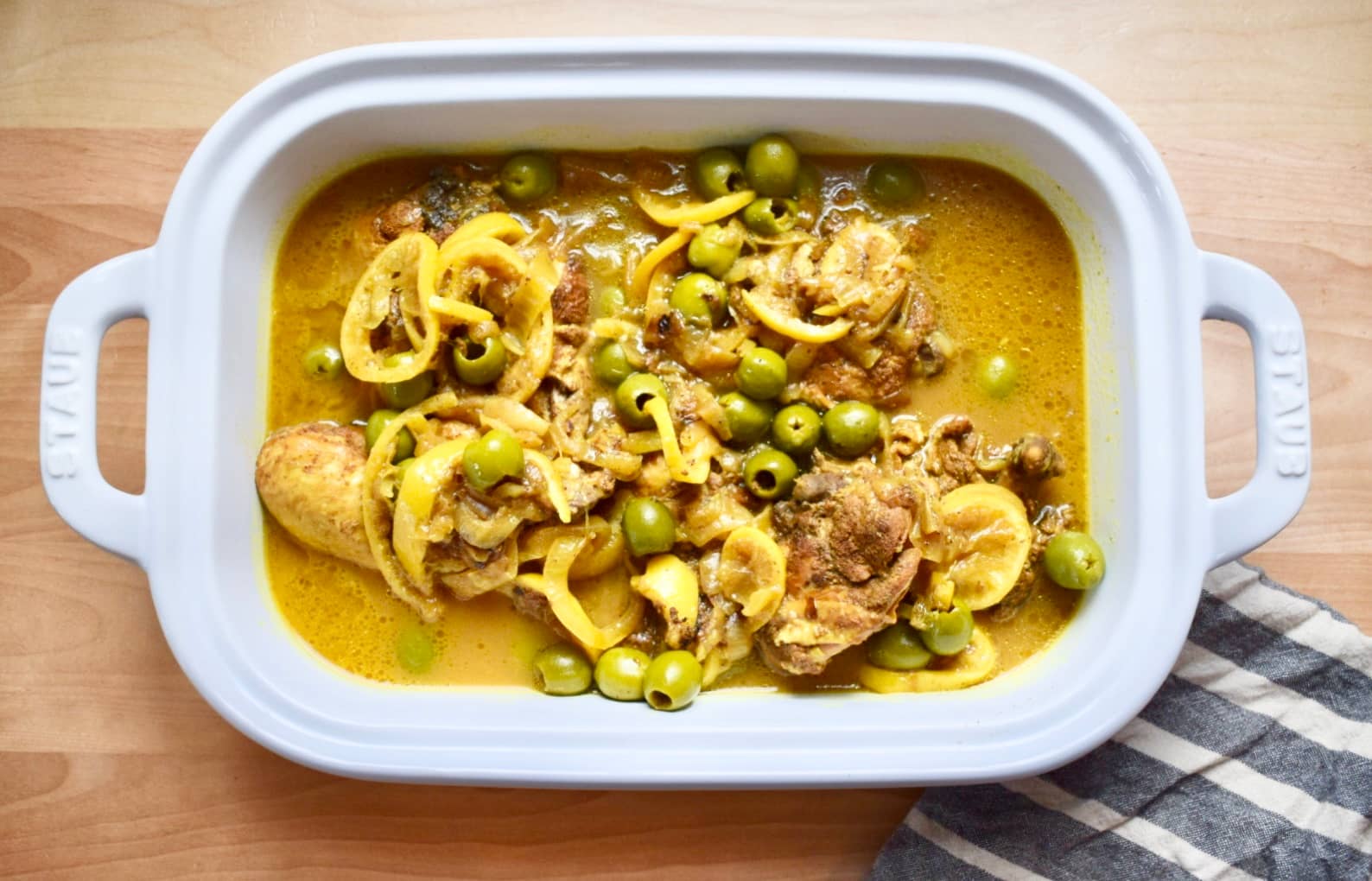 Moroccan-spiced chicken covered in lemons and olives in a white serving tray with golden juices