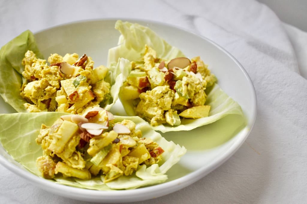 White ceramic bowl with three lettuce cups with a scoop of healthy curry chicken salad and sliced almonds on top.