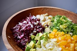 Chicory salad in large wooden bowl. Radicchio, endive, hearts of palm, avocado, frisee lettuce, and orange.