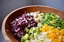Chicory salad in large wooden bowl. Radicchio, endive, hearts of palm, avocado, frisee lettuce, and orange.
