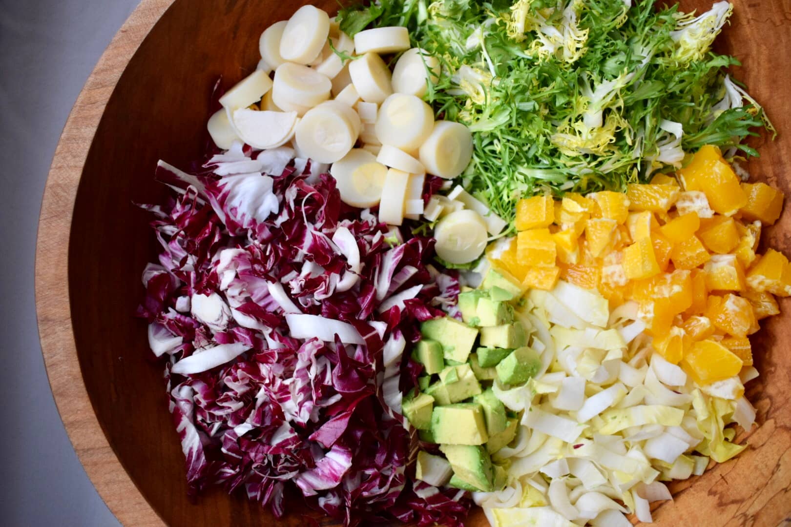 Chicory salad in large wooden bowl. Radicchio, endive, hearts of palm, avocado, frisee lettuce, and orange.