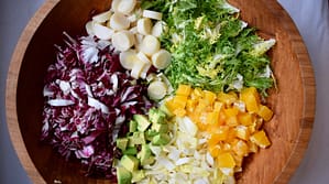 Chicory salad in large wooden bowl. Radicchio, endive, hearts of palm, avocado, frisee lettuce, and orange.